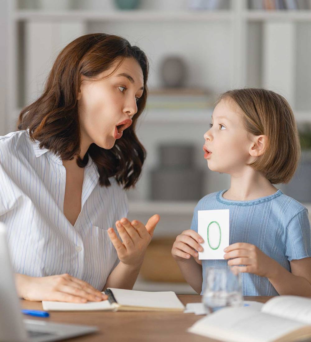 Speech therapist demonstrating mouth positions to a young girl during an articulation therapy session